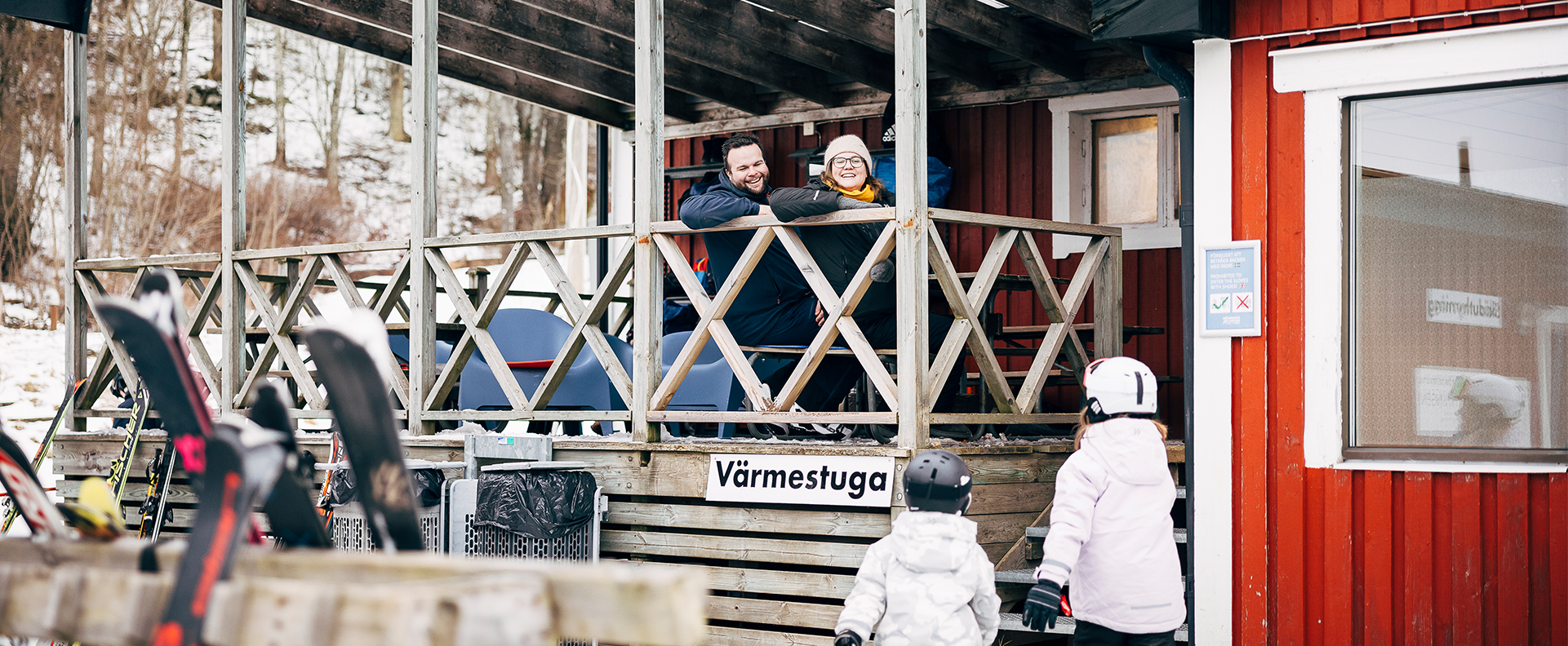 Woman and man sitting on the veranda of the warming house. Two children stand below.