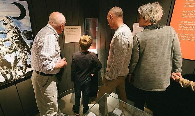 en farfar/morfar, en pappa, ett pojke, en mamma sår med ryggen mot kameran och kikar på en museimonter. Alla har ljusa kläder utom pojken som har grå